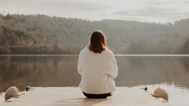A woman sitting on a dock looking out over a lake.