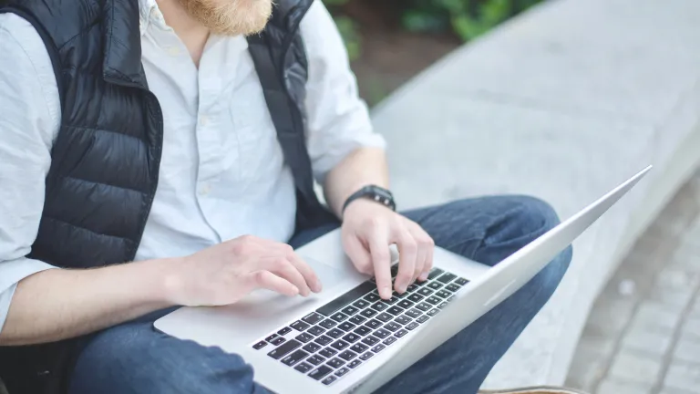 A man typing on a laptop on his lap.