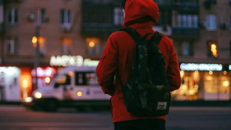 A person wearing a jacket and backpack walking in a city.