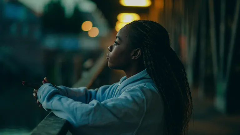 A young woman looking out over a view with arms resting on a banister.