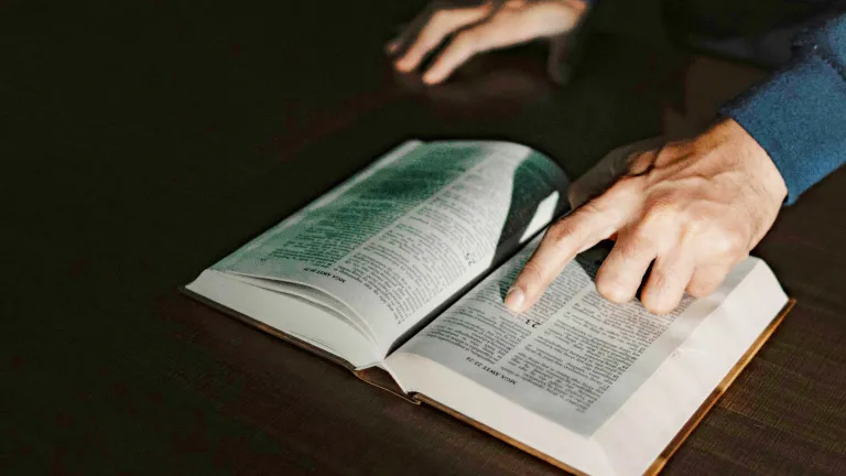 a hand pointing to a verse in an open Bible