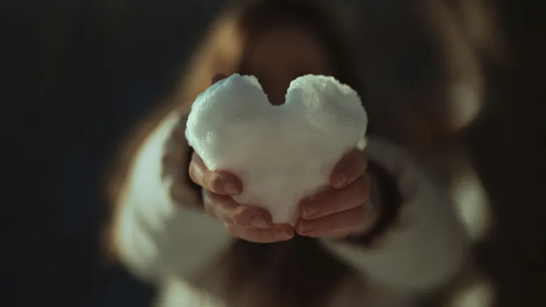a pair of hands holding a heart made of snow
