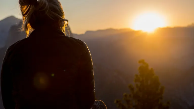 A person looking at the sun going down over a mountain.