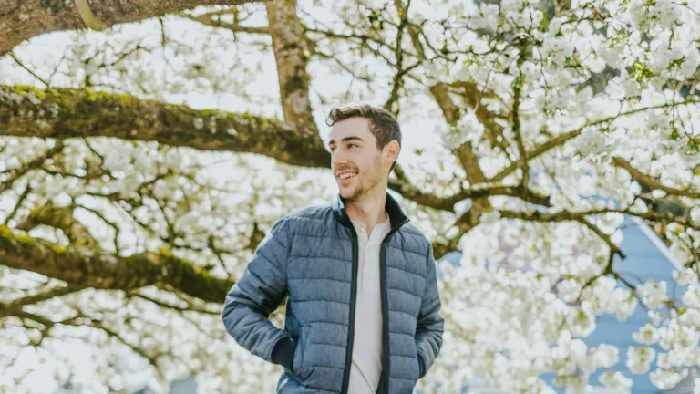 a man walking underneath tree branches covered in white blossoms