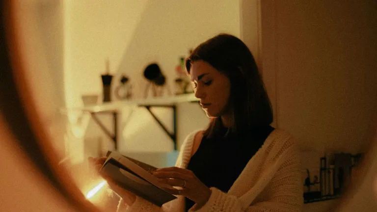a woman holding a book, reflected in a mirror