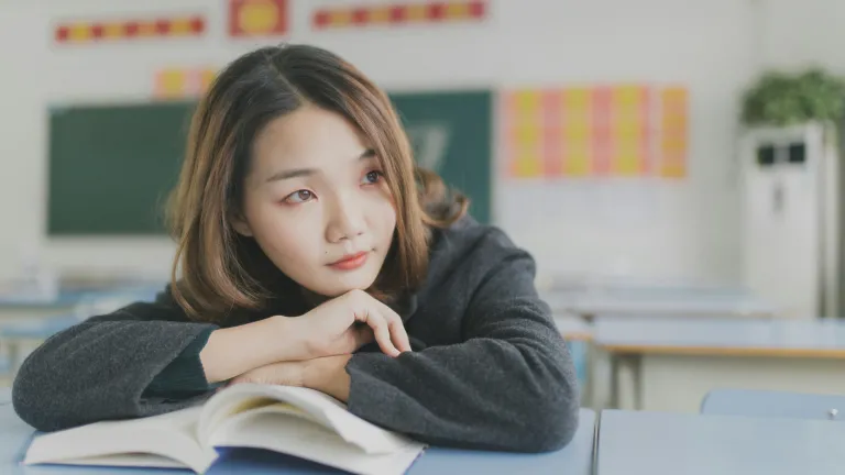 a woman leaning on an open book while sitting in a classroom