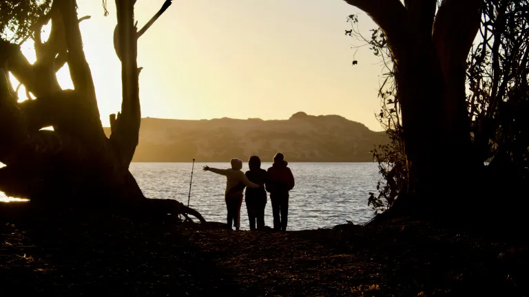 True joy is a steadfast, Spirit-imbued inner strength and enduring hope that persists through trials and suffering, growing through relationship with God and enabling us to radiate His presence to others. Three people watching the glow of the sun while they are standing by a lake.