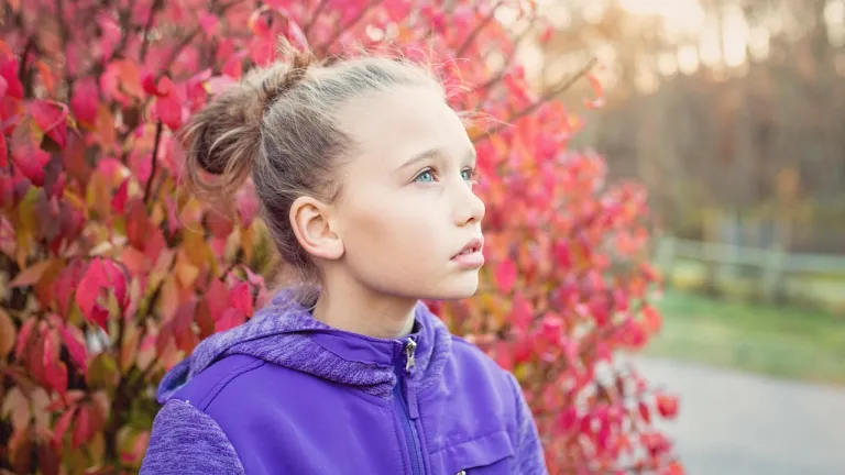a girl who looks concerned standing in front of a bush with red leaves