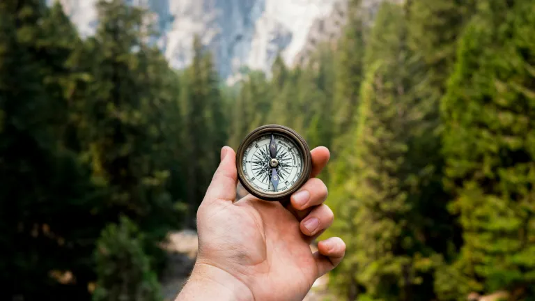 a hand holding a compass with mountains in the background