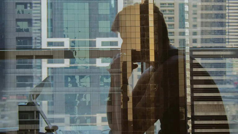 The reflection of man sitting and staring at his laptop computer.