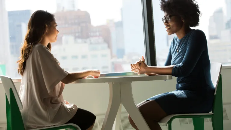 Two young women talking at a small table.