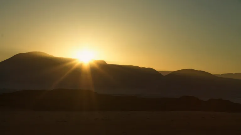 The Kingdom of God is not yet here in fullness, but today we can choose to live under Christ’s reign as we await His glorious return. The sun setting over a mountain range.
