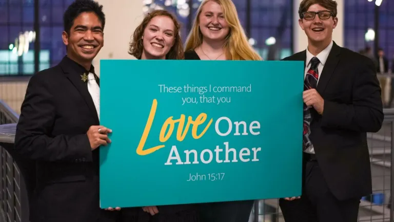 four young adults holding a "love one another" sign