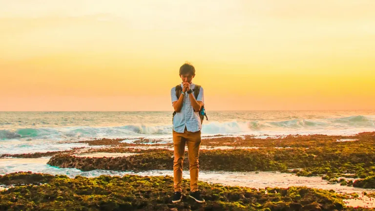 a man praying with a body of water and sunset in the background