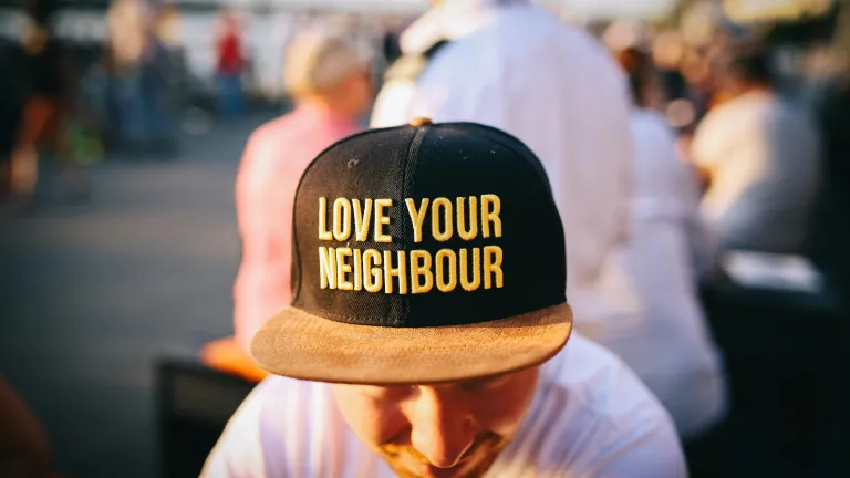 “Not everyone who says to Me, ‘Lord, Lord,’ shall enter the kingdom of heaven, but he who does the will of My Father in heaven” (Matthew 7:21) A person wearing a hat that says "Love Your Neighbor"