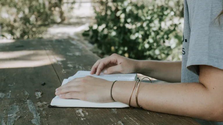 When it comes to our spiritual diet, what do we eat? a woman's arms resting on an open Bible outdoors on a wooden table