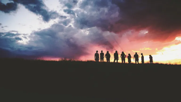 Silhouette of nine persons standing on the hill.