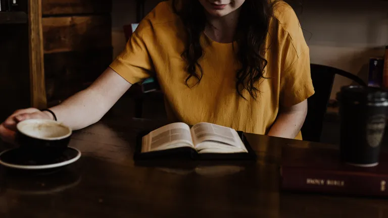 We obey God as an outward sign of our love, obedience and commitment to Him. a woman sitting at a table with an open Bible and a coffee mug