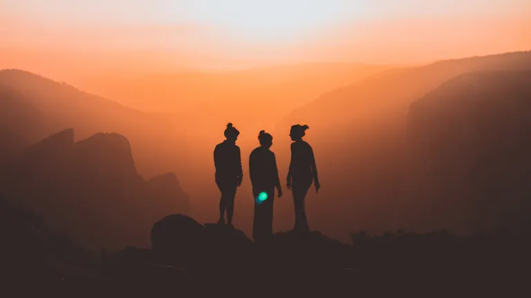the silhouettes of three women against a backdrop of mountains at sunset.