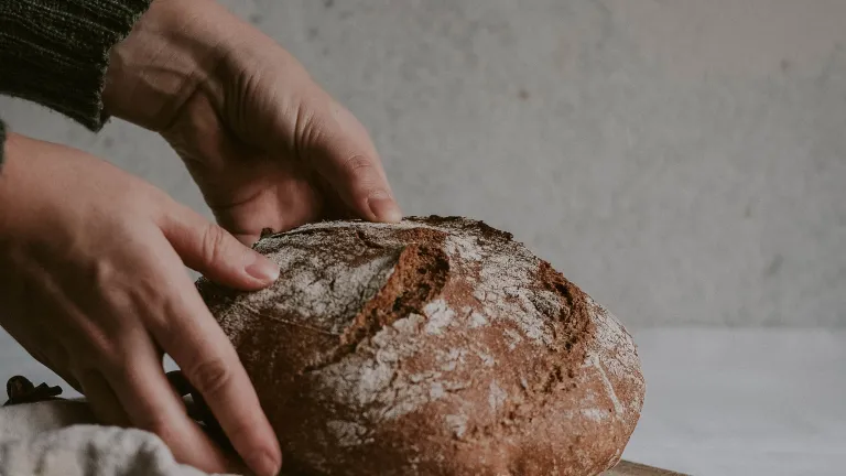 a pair of hands placing a loaf of bread onto a wooden cutting board