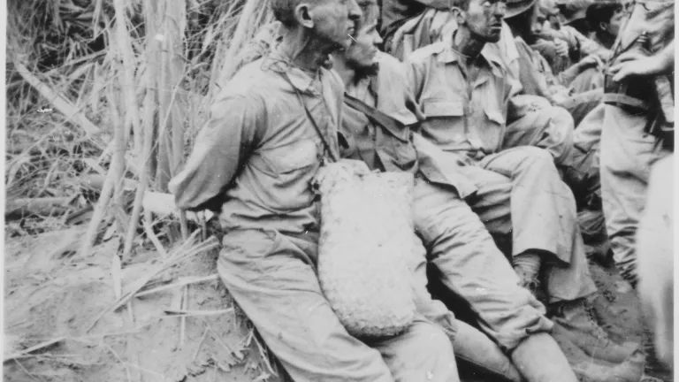 black and white scene of several prisoners seated with hands tied behind their backs