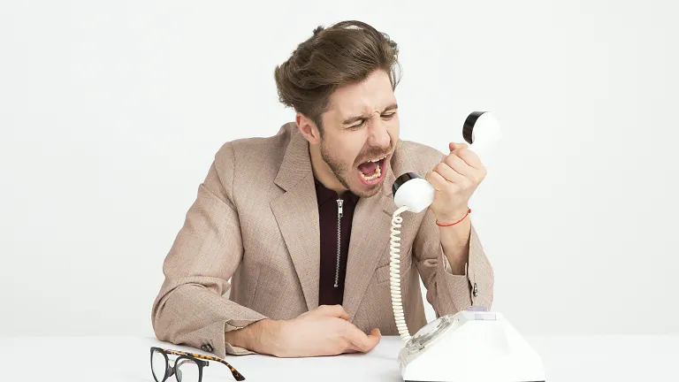 an angry man yelling into the receiver of a phone