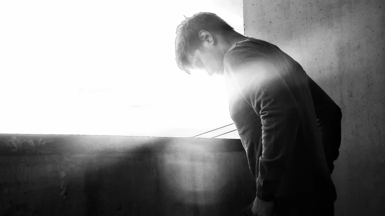 A man looking down as the sun glares in the background.