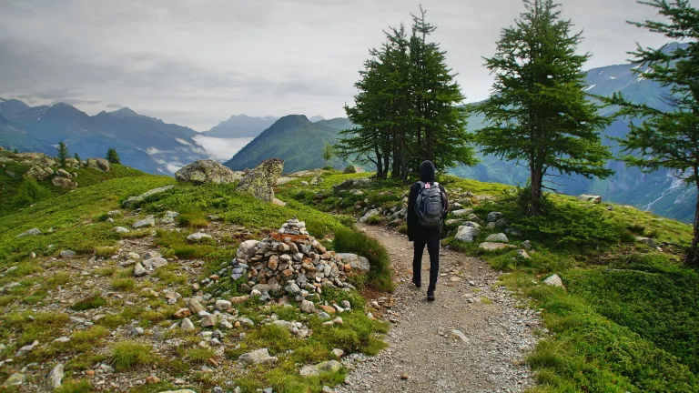 a man walking on a mountain trail looking out at the peaks in the horizon