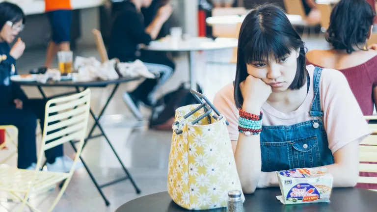 a sad woman sitting alone at a table in a college cafeteria
