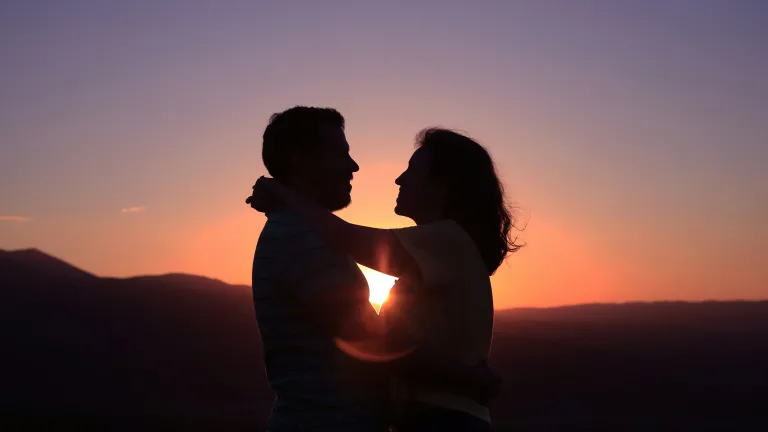 a silhouette of a man and a woman hugging with the sunset in the background