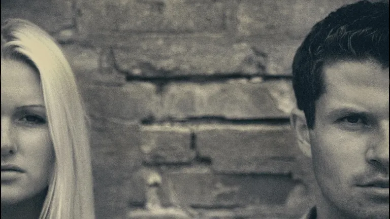 half of a woman's face and half of a man's face in grayscale separated by an expanse of brick wall