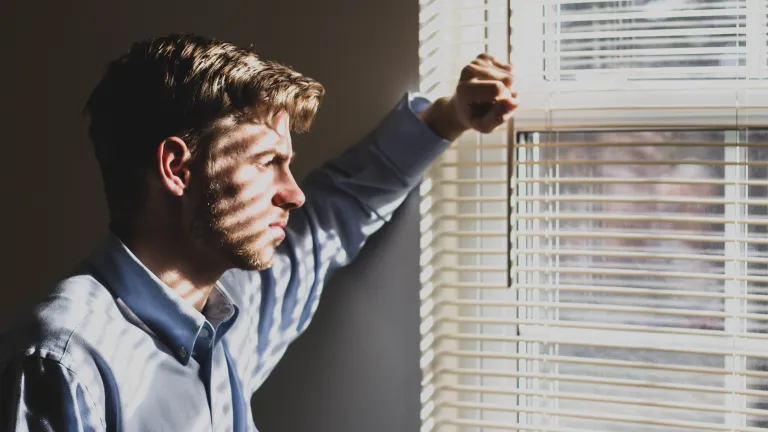 How can we trust God when many times we just don't understand what He's doing? a man lifting a slat on the set of blinds on a window to look outside