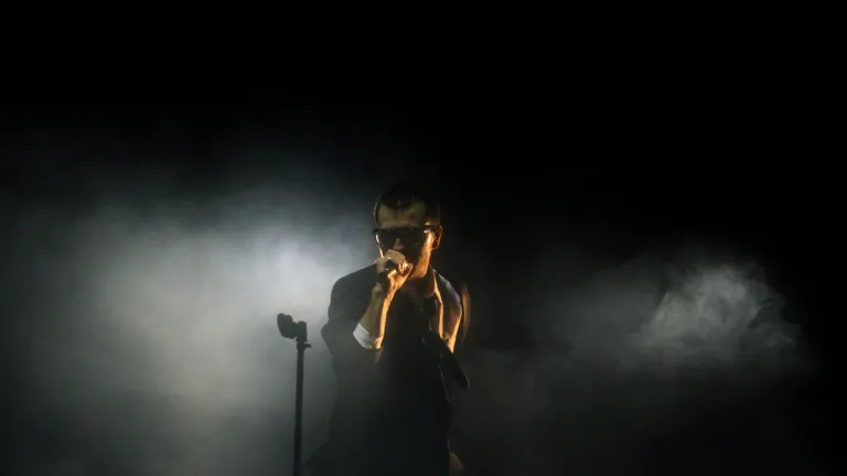 Hard-core coolness is an expression of feeling self-confident and superior to others. A man singing into a microphone on dark foggy stage.