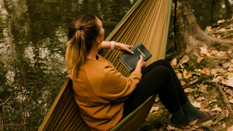 a woman sitting in a hammock and holding a Bible