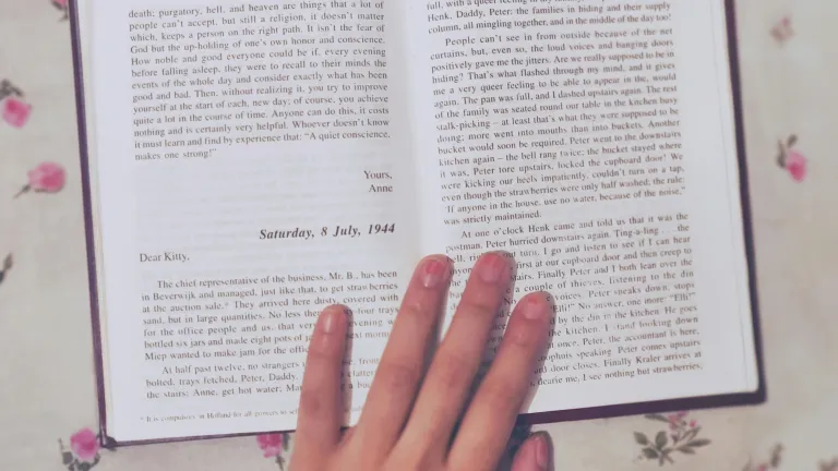 a book held open with a hand on a table covered with a flowered tablecloth