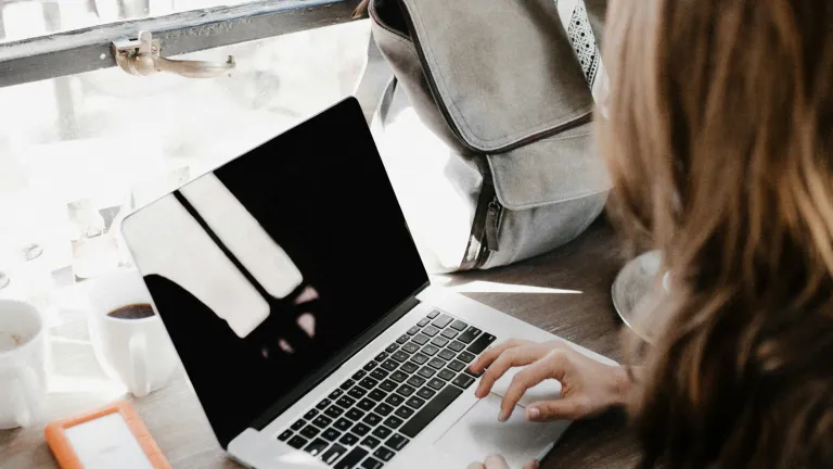 A woman seated with an open laptop and a backpack on the desk in front of her