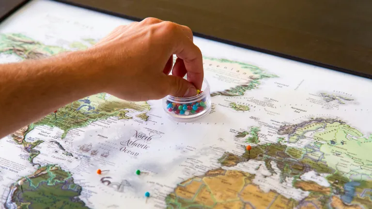 a hand reaching into a plastic container of colorful pins sitting atop a world map