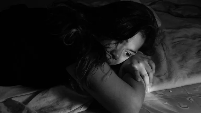 A woman laying on a bed looking depressed.