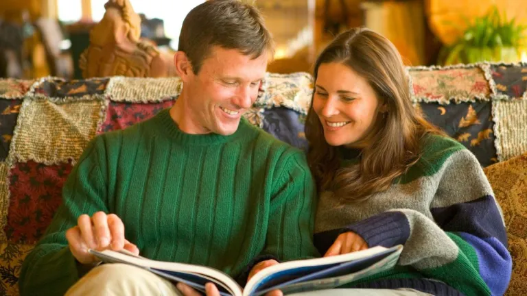 Two people must learn to work together in marriage, showing respect and love to each other. A couple sitting together on a couch looking at a large book.