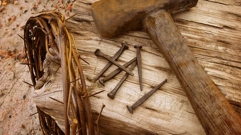 Photo illustration of a crown of thorns, old nails, hammer and wood beam.