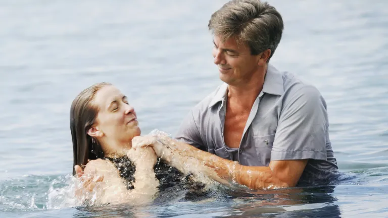 A man baptizing a woman after being fully submersed in the water.
