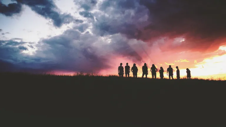 A group of people standing on top of a hill with the sun setting in the background.
