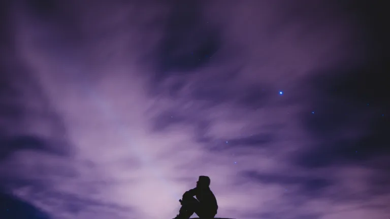 A person sitting on a hill with the stars in background.