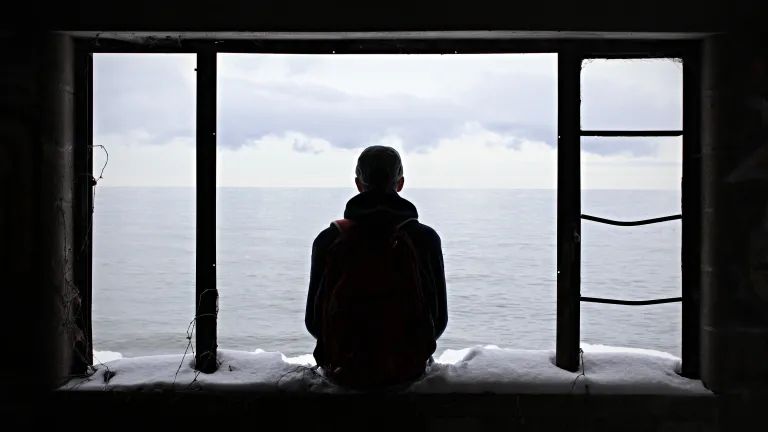 A teen sitting in abandoned window frame of an old house.