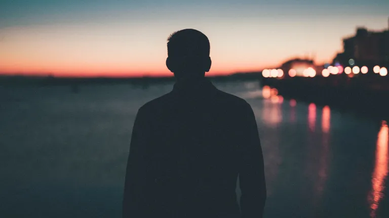 A silhouette of young man looking out over a body of water.