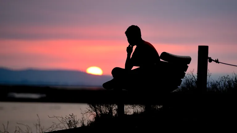 A person sitting on a bench with the sun setting.