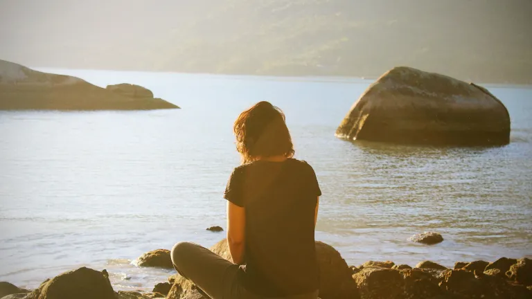 We are filled with joy and peace. A woman sitting by a body of water.