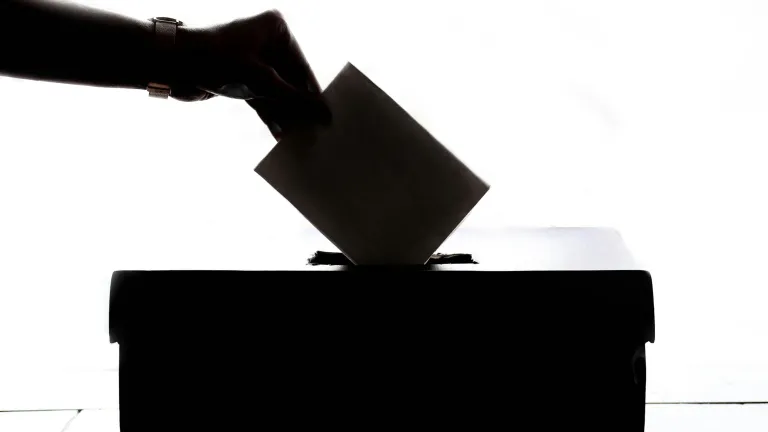 A photo illustration of hand inserting a vote card into a box.