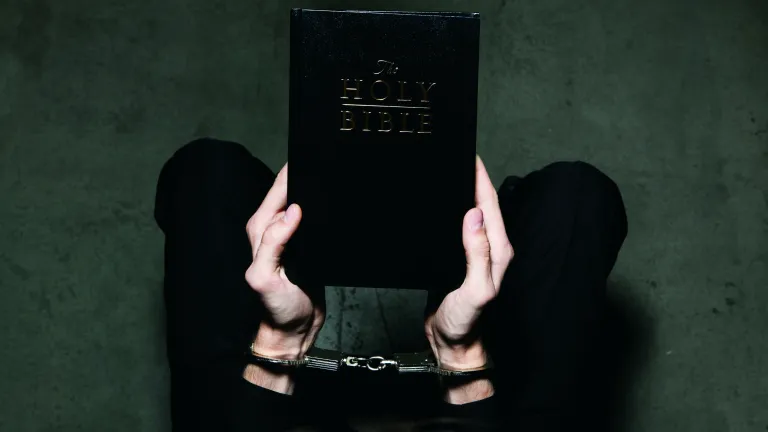 Without God, we are slaves to the downward pulls of our own human nature. A person holding a Bible while their hands are wearing shackles.