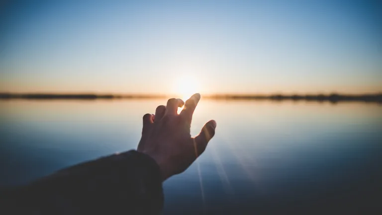 A hand reaching out over water.